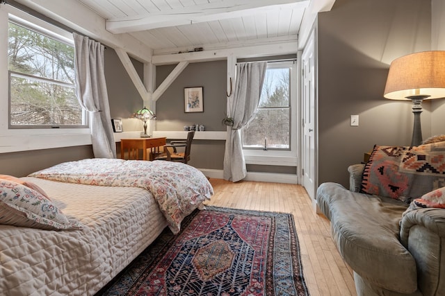 bedroom featuring beamed ceiling, wood ceiling, multiple windows, and light wood-type flooring