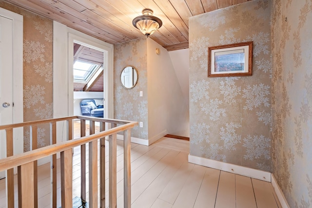 hall featuring a skylight, light hardwood / wood-style floors, and wooden ceiling