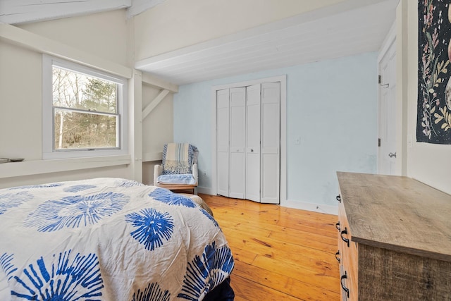 bedroom with lofted ceiling with beams, hardwood / wood-style floors, and a closet