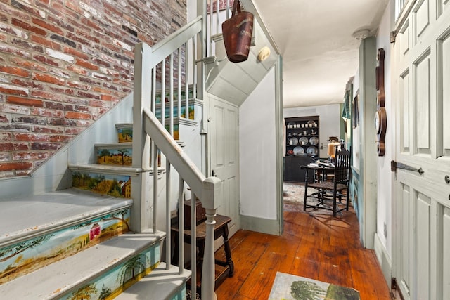 stairway with hardwood / wood-style flooring and brick wall