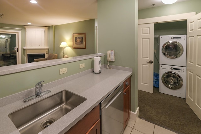 kitchen featuring a fireplace, dishwasher, sink, stacked washer and clothes dryer, and light tile patterned floors