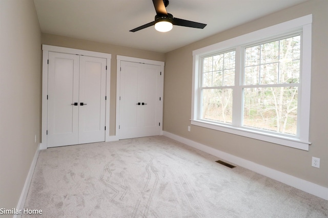 unfurnished bedroom featuring multiple closets, light colored carpet, and ceiling fan