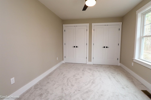 unfurnished bedroom featuring multiple closets, ceiling fan, light colored carpet, and multiple windows