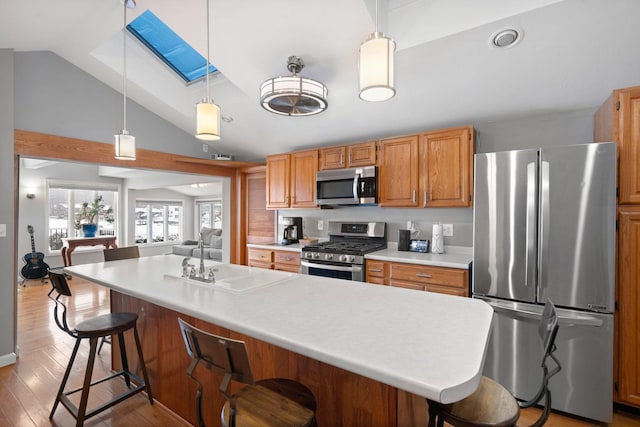 kitchen featuring sink, decorative light fixtures, appliances with stainless steel finishes, a kitchen breakfast bar, and vaulted ceiling with skylight