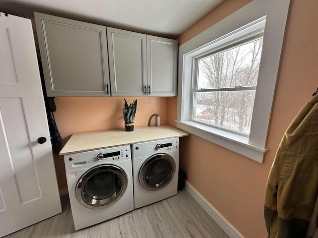 clothes washing area featuring cabinets, washing machine and clothes dryer, and light wood-type flooring