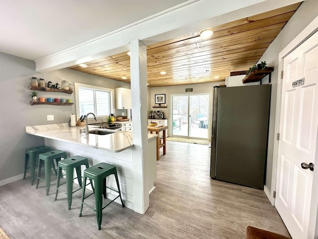 kitchen with a breakfast bar, sink, white cabinetry, light hardwood / wood-style flooring, and stainless steel refrigerator