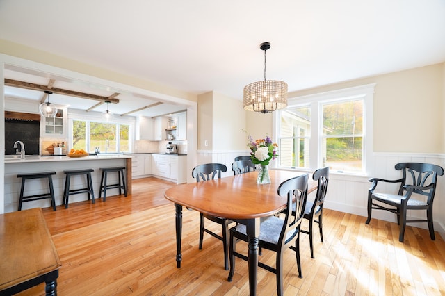 dining room with sink, a chandelier, beamed ceiling, and light wood-type flooring