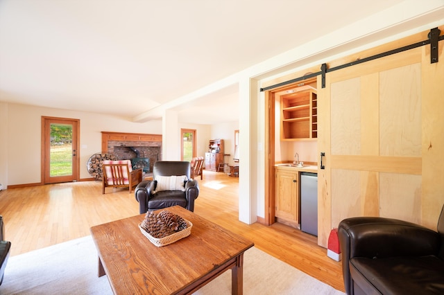 living room featuring a fireplace, a barn door, light hardwood / wood-style flooring, and wet bar