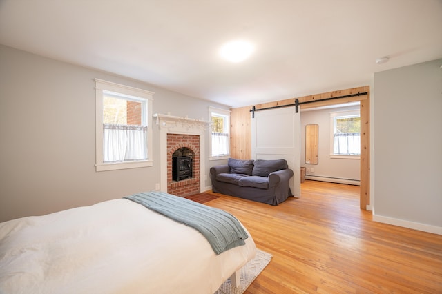 bedroom featuring a barn door, light wood-type flooring, a brick fireplace, and a baseboard heating unit