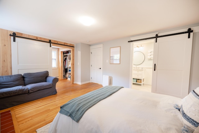 bedroom featuring radiator, hardwood / wood-style floors, a barn door, ensuite bath, and a closet