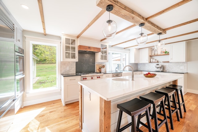 kitchen with sink, white cabinetry, hanging light fixtures, light hardwood / wood-style flooring, and an island with sink