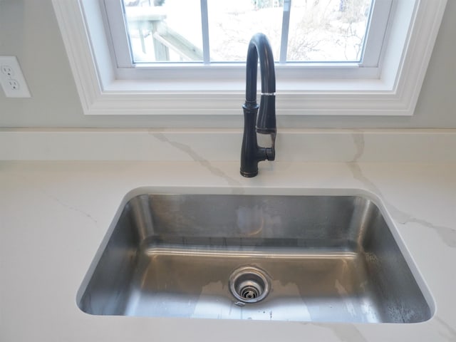 interior details with white cabinetry, sink, and light stone counters