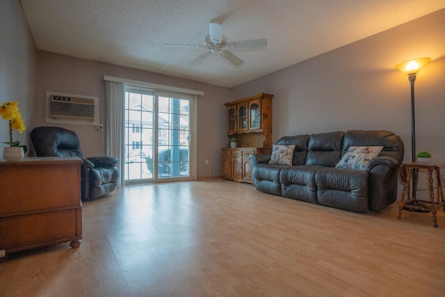 living room featuring ceiling fan, a wall mounted air conditioner, light hardwood / wood-style flooring, and a textured ceiling