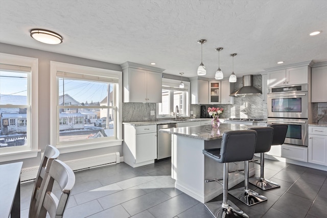 kitchen featuring a kitchen island, pendant lighting, a baseboard radiator, stainless steel appliances, and wall chimney exhaust hood