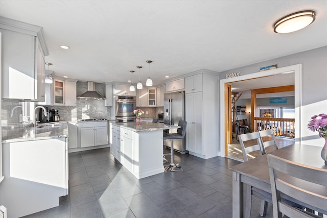 kitchen with wall chimney exhaust hood, sink, a center island, hanging light fixtures, and stainless steel appliances