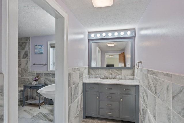 bathroom featuring vanity, a textured ceiling, and tile walls