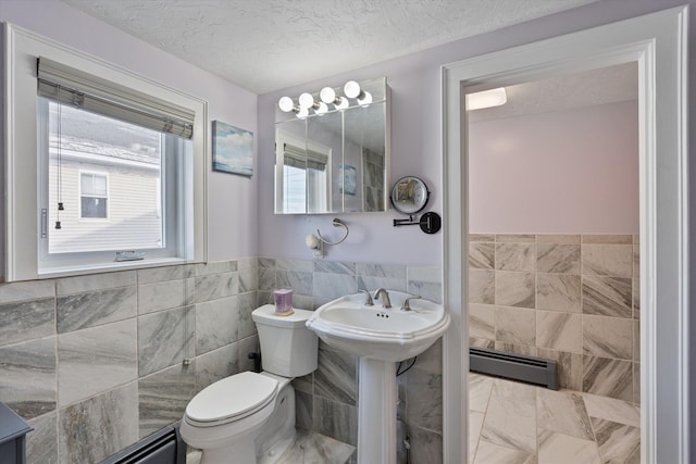 bathroom featuring sink, tile walls, baseboard heating, toilet, and a textured ceiling