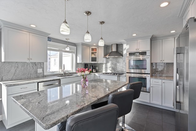 kitchen with appliances with stainless steel finishes, decorative light fixtures, sink, a center island, and wall chimney exhaust hood