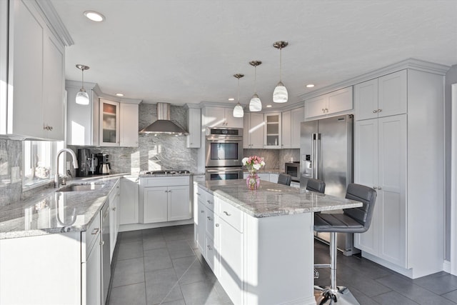 kitchen with pendant lighting, sink, wall chimney exhaust hood, and appliances with stainless steel finishes