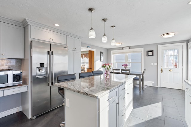 kitchen with backsplash, hanging light fixtures, light stone counters, a kitchen island, and stainless steel fridge with ice dispenser