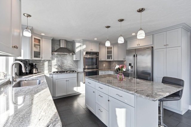 kitchen with hanging light fixtures, appliances with stainless steel finishes, sink, and wall chimney range hood