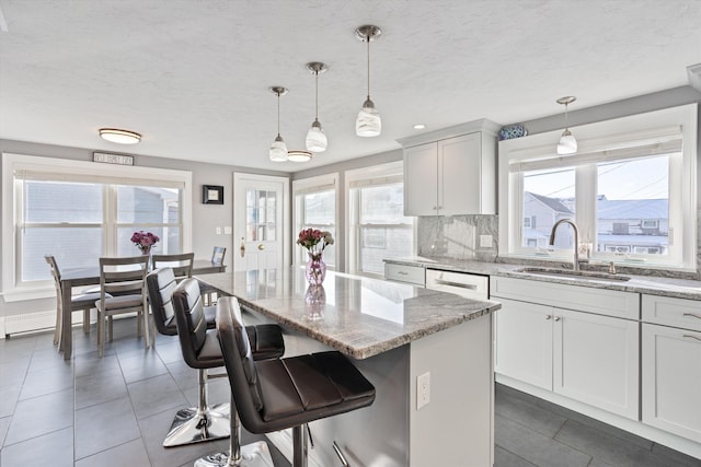 kitchen featuring pendant lighting, sink, light stone counters, a kitchen island, and decorative backsplash