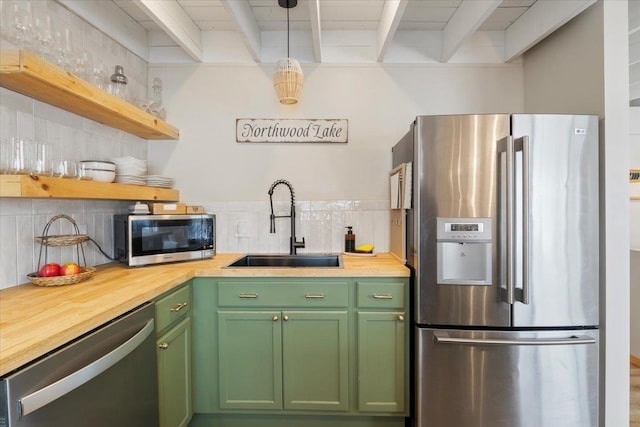 kitchen with appliances with stainless steel finishes, sink, pendant lighting, and wood counters