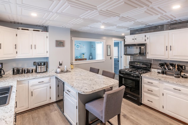 kitchen with white cabinets, a kitchen breakfast bar, light wood-type flooring, and black appliances