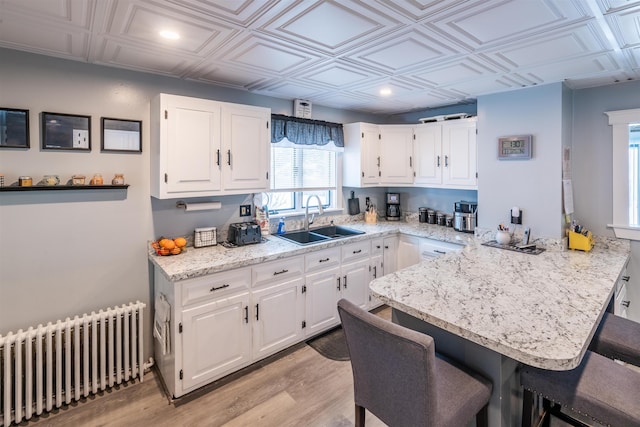 kitchen with light stone countertops, sink, radiator heating unit, and white cabinets