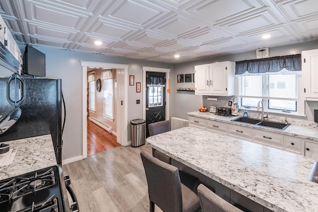 kitchen with radiator heating unit, white cabinetry, sink, baseboard heating, and light wood-type flooring