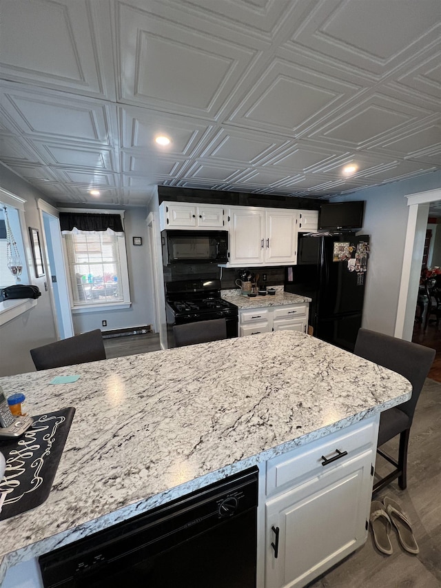 kitchen featuring a kitchen bar, wood-type flooring, white cabinets, light stone countertops, and black appliances