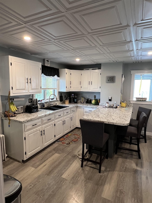 kitchen featuring white cabinetry, wood-type flooring, sink, a kitchen bar, and light stone countertops