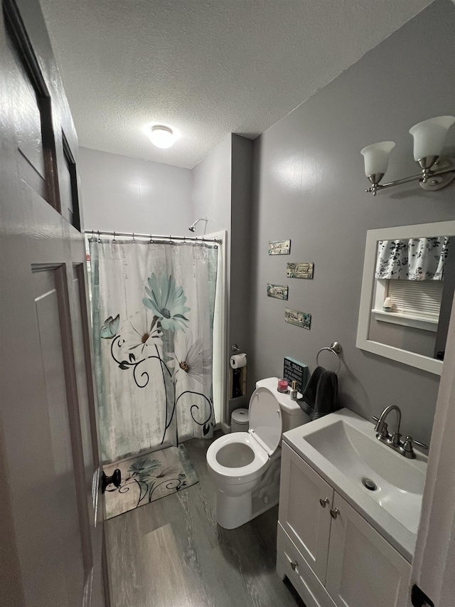 bathroom featuring walk in shower, toilet, wood-type flooring, a textured ceiling, and vanity