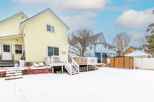 snow covered house with a wooden deck and a storage shed