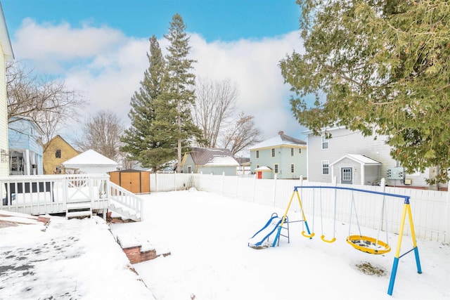 snowy yard with a wooden deck and a playground