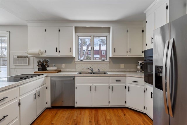 kitchen with a wall mounted air conditioner, sink, white cabinets, stainless steel appliances, and light wood-type flooring