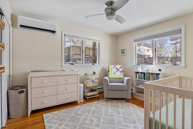 bedroom featuring light hardwood / wood-style flooring, an AC wall unit, a baseboard radiator, ceiling fan, and a crib