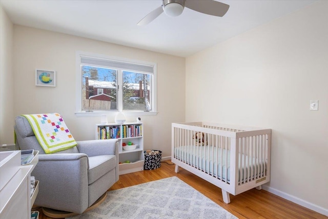 bedroom featuring a nursery area, ceiling fan, and light hardwood / wood-style flooring