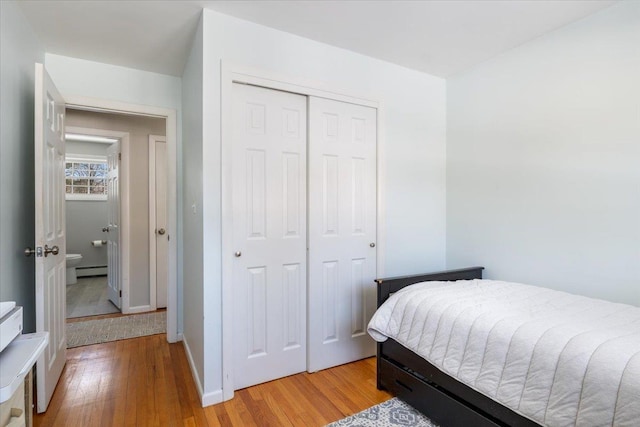 bedroom featuring baseboard heating, light hardwood / wood-style floors, and a closet