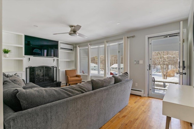 living room featuring ceiling fan, baseboard heating, a brick fireplace, a wall unit AC, and light hardwood / wood-style flooring