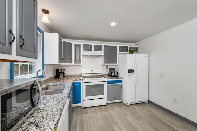 kitchen with sink, gray cabinetry, light wood-type flooring, light stone counters, and white appliances