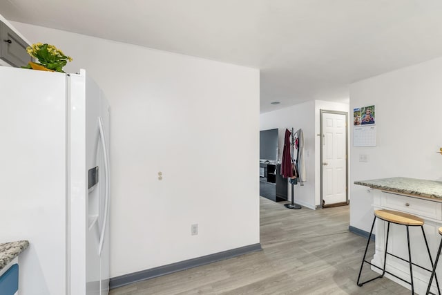 kitchen with a breakfast bar, light stone countertops, light hardwood / wood-style floors, and white fridge with ice dispenser