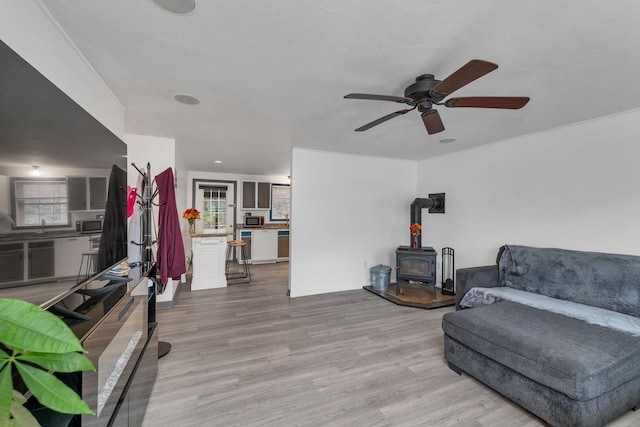 living room with ceiling fan, sink, light hardwood / wood-style flooring, and a wood stove