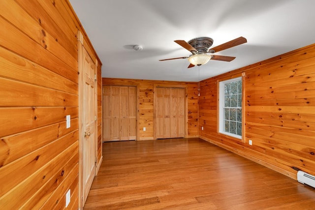 unfurnished room featuring baseboard heating, ceiling fan, light hardwood / wood-style floors, and wood walls