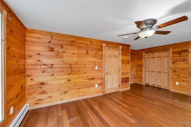 spare room with wood-type flooring, ceiling fan, baseboard heating, and wood walls