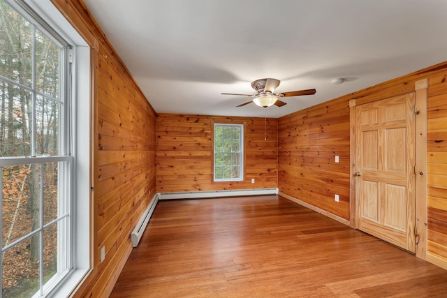 empty room featuring ceiling fan, a baseboard heating unit, wooden walls, and light hardwood / wood-style flooring