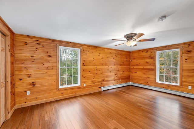 empty room featuring ceiling fan, a baseboard radiator, a healthy amount of sunlight, and wood-type flooring