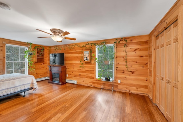 bedroom with hardwood / wood-style flooring, wood walls, ceiling fan, and a baseboard heating unit