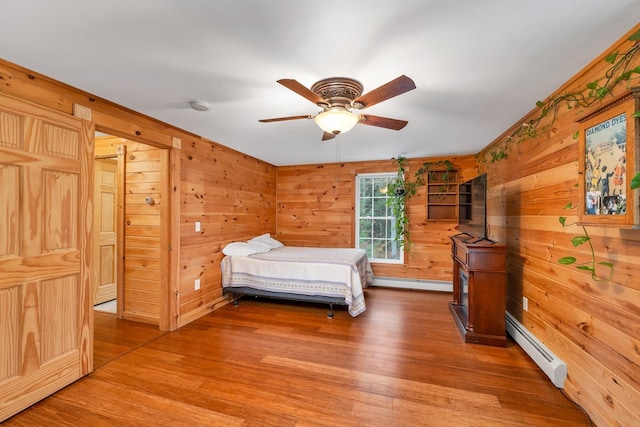 unfurnished bedroom with wood-type flooring, a baseboard heating unit, ceiling fan, and wood walls