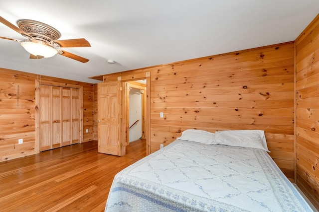 bedroom featuring ceiling fan, wood-type flooring, and wooden walls